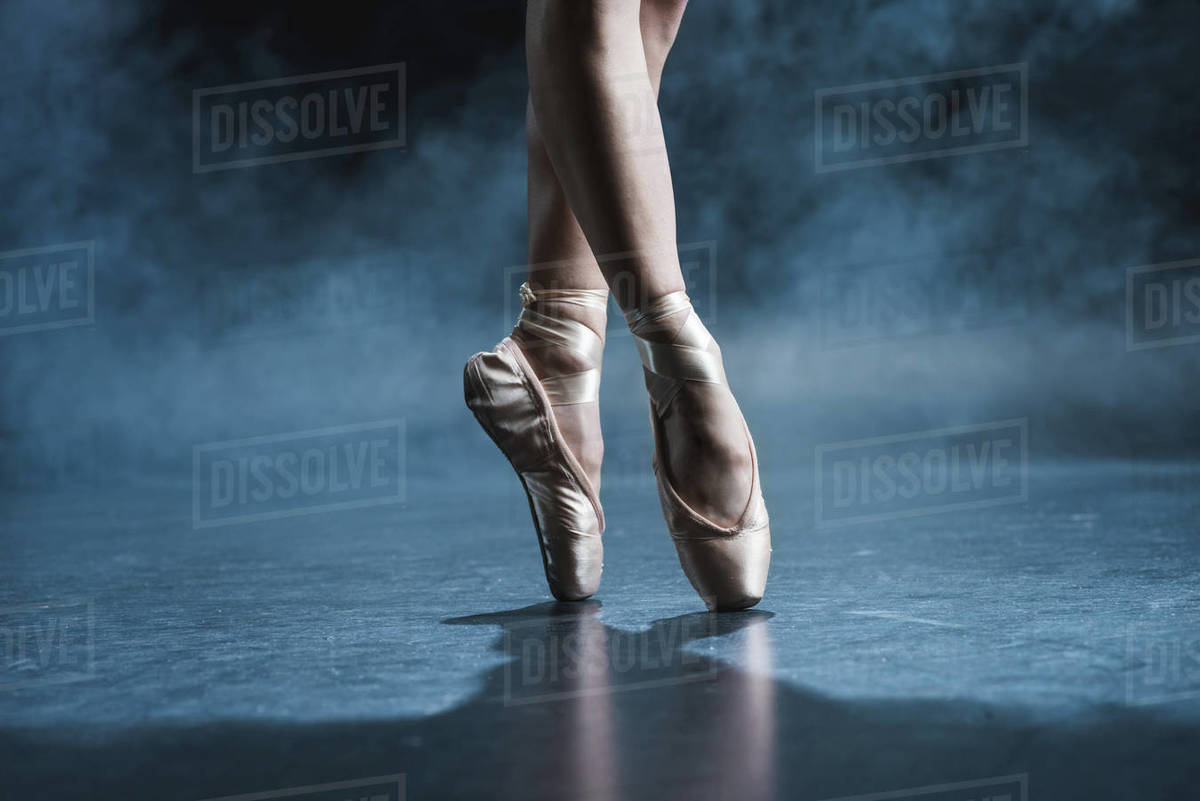Cropped view of ballet dancer in pointe shoes in dark studio with
