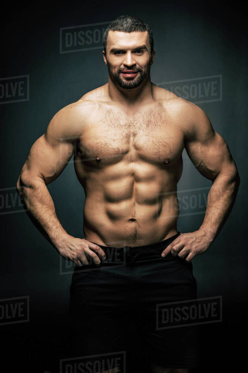 Portrait of shirtless sportive man standing akimbo isolated on black