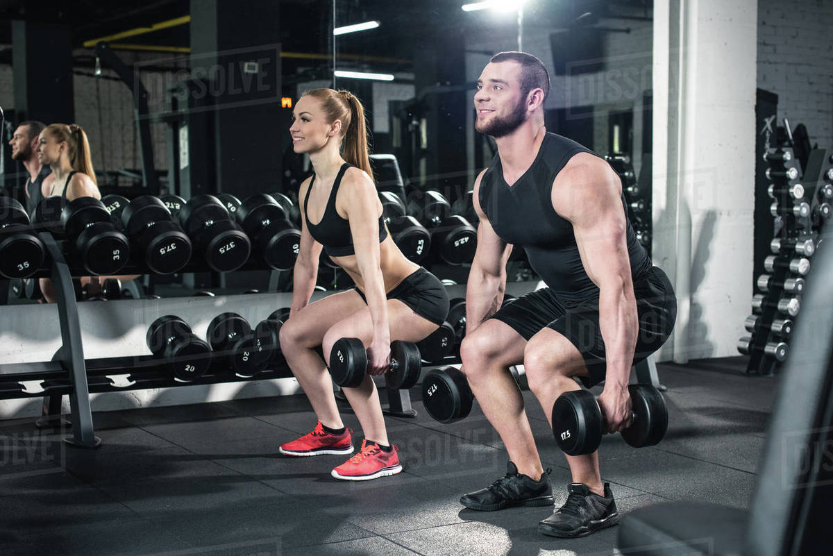 Side view of couple exercising with dumbbells together at gym Stock