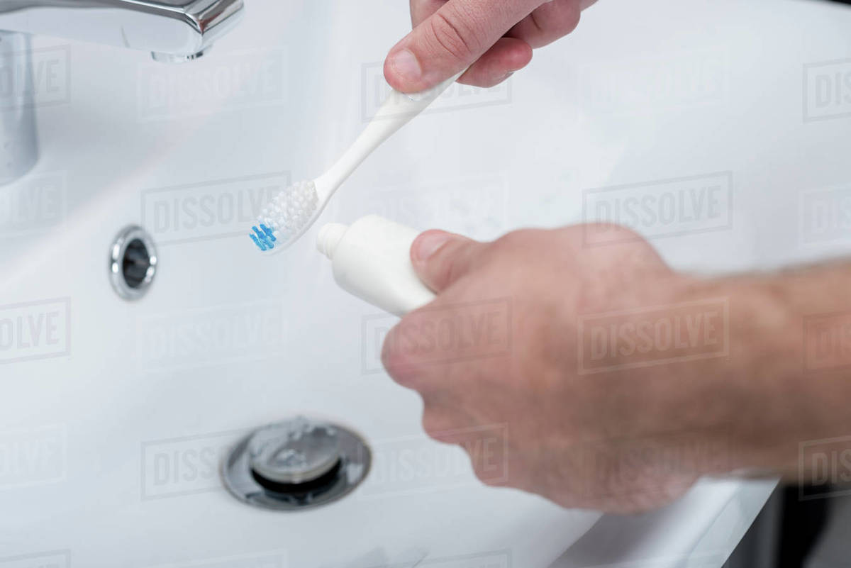 Cropped shot of man applying toothpaste on toothbrush in bathroom