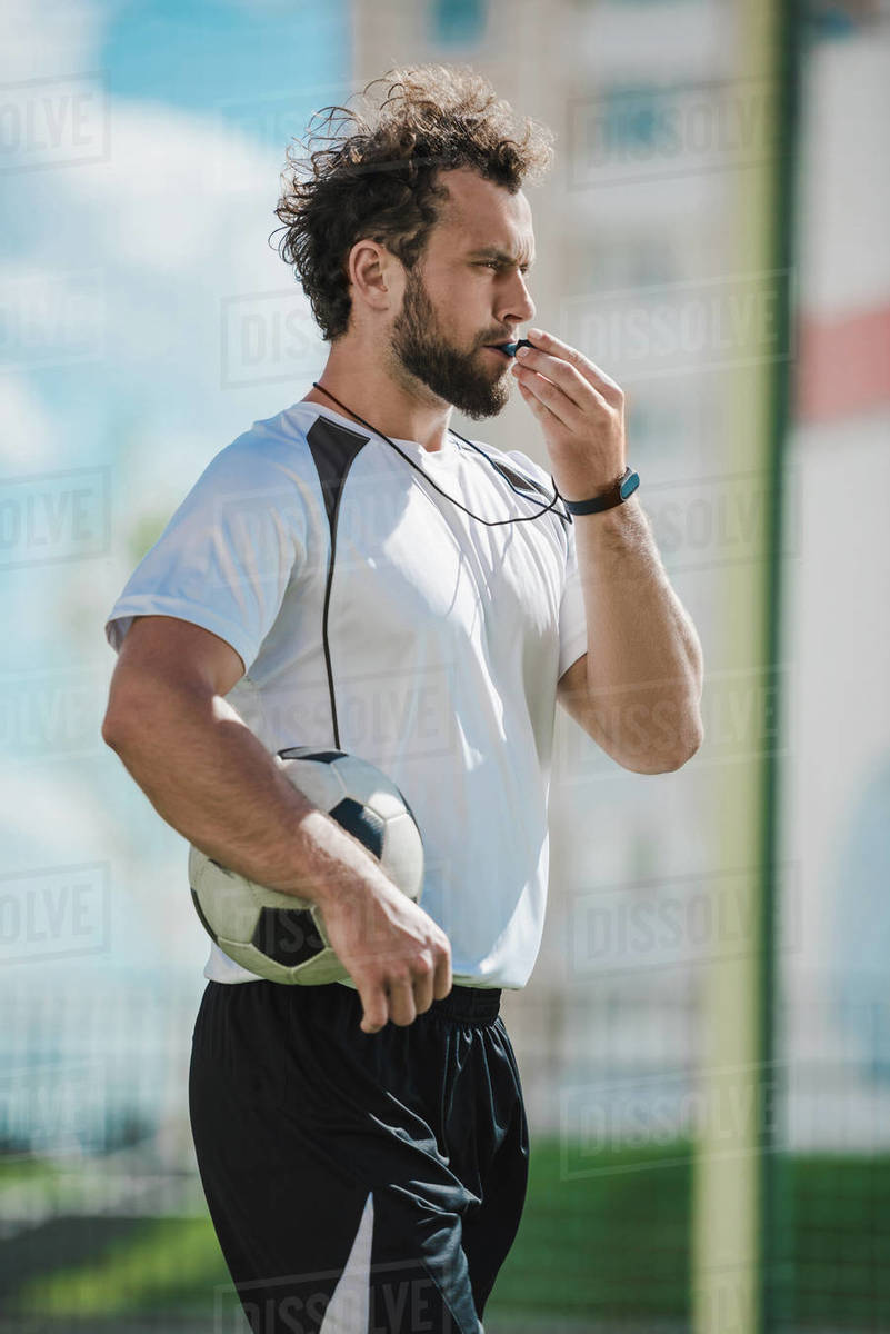 Side view of soccer referee whistling in whistle on soccer pitch during