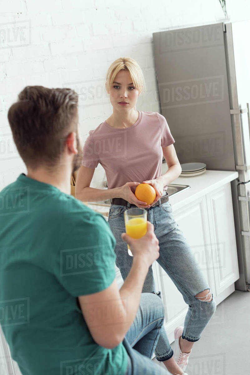 Couple of vegans talking in kitchen and holding orange and orange juice