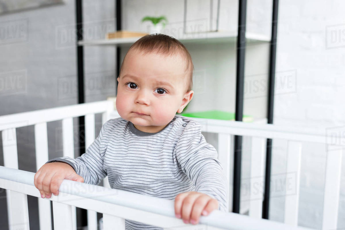 Closeup portrait of cute little child in baby cot looking at camera