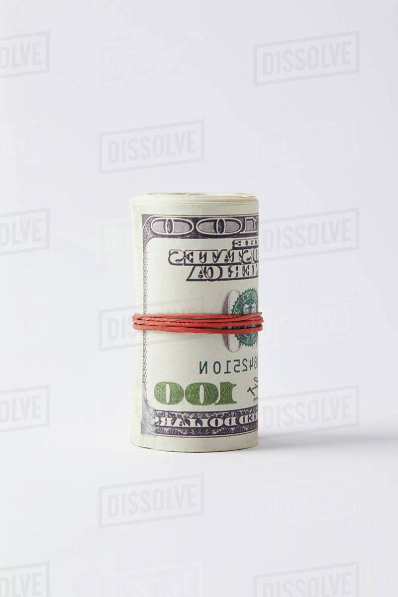 Roll of dollars tied with rubber band on white surface Stock Photo