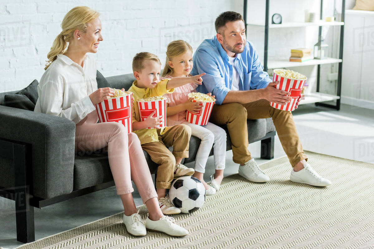 Family with two kids eating popcorn and watching tv at home Stock