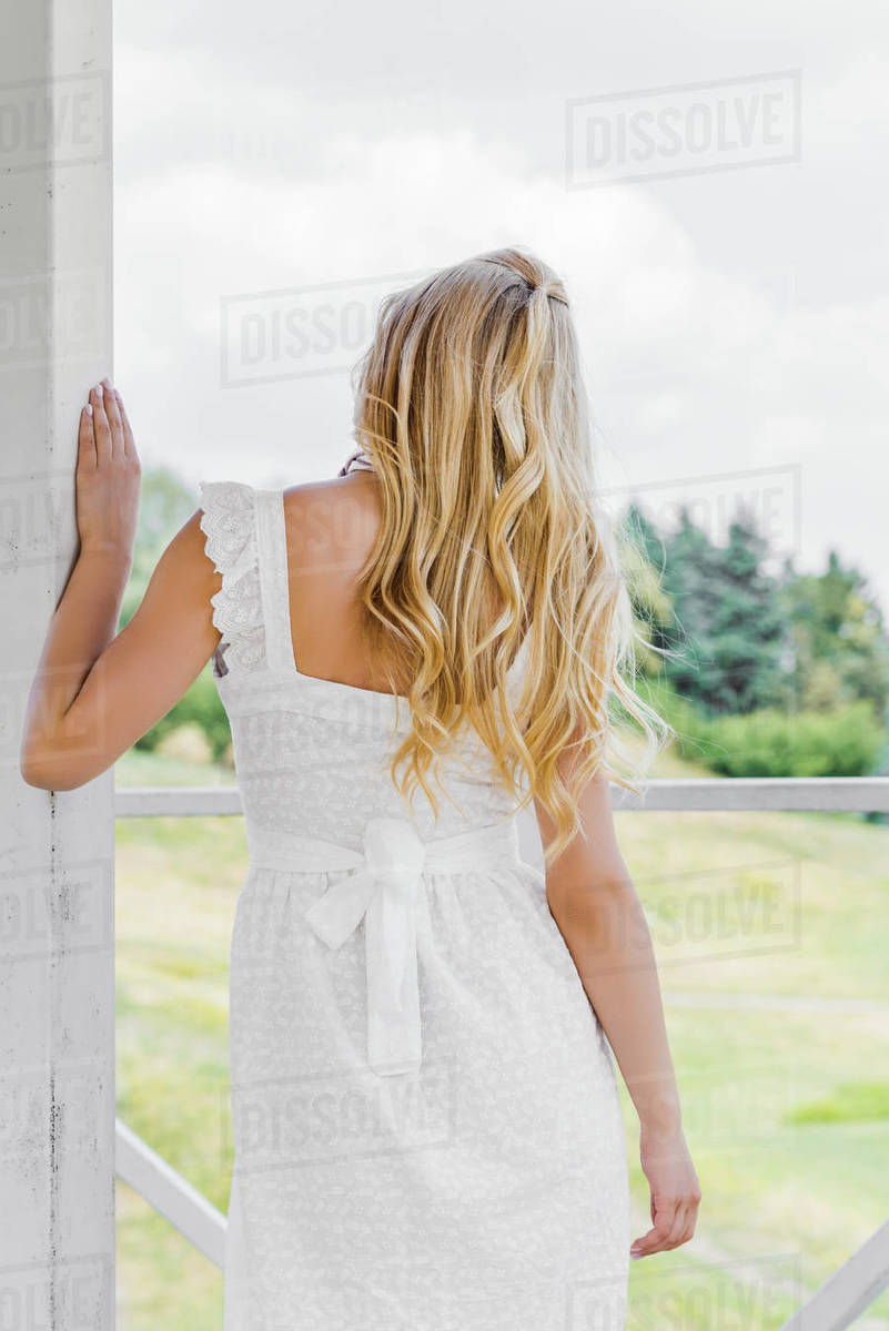 Back view of beautiful blonde girl in white dress looking at green