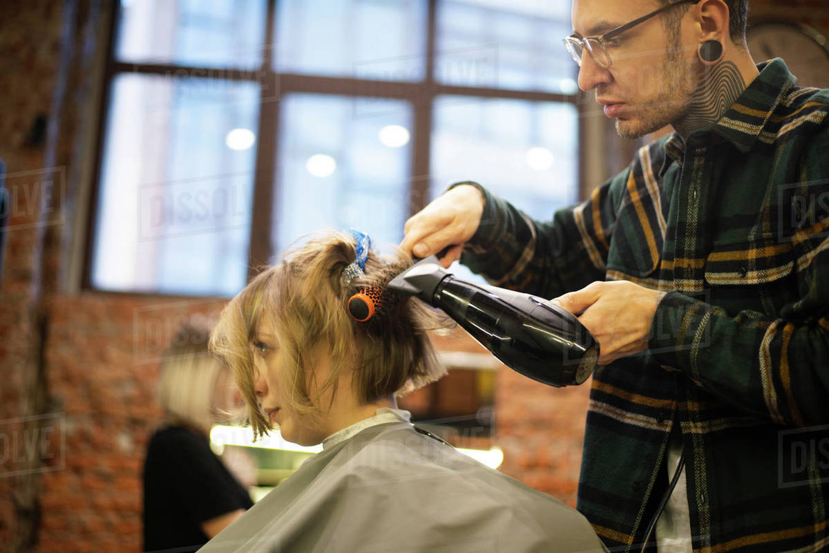 Hairdresser drying customer's hair by a hair dryer in salon Stock