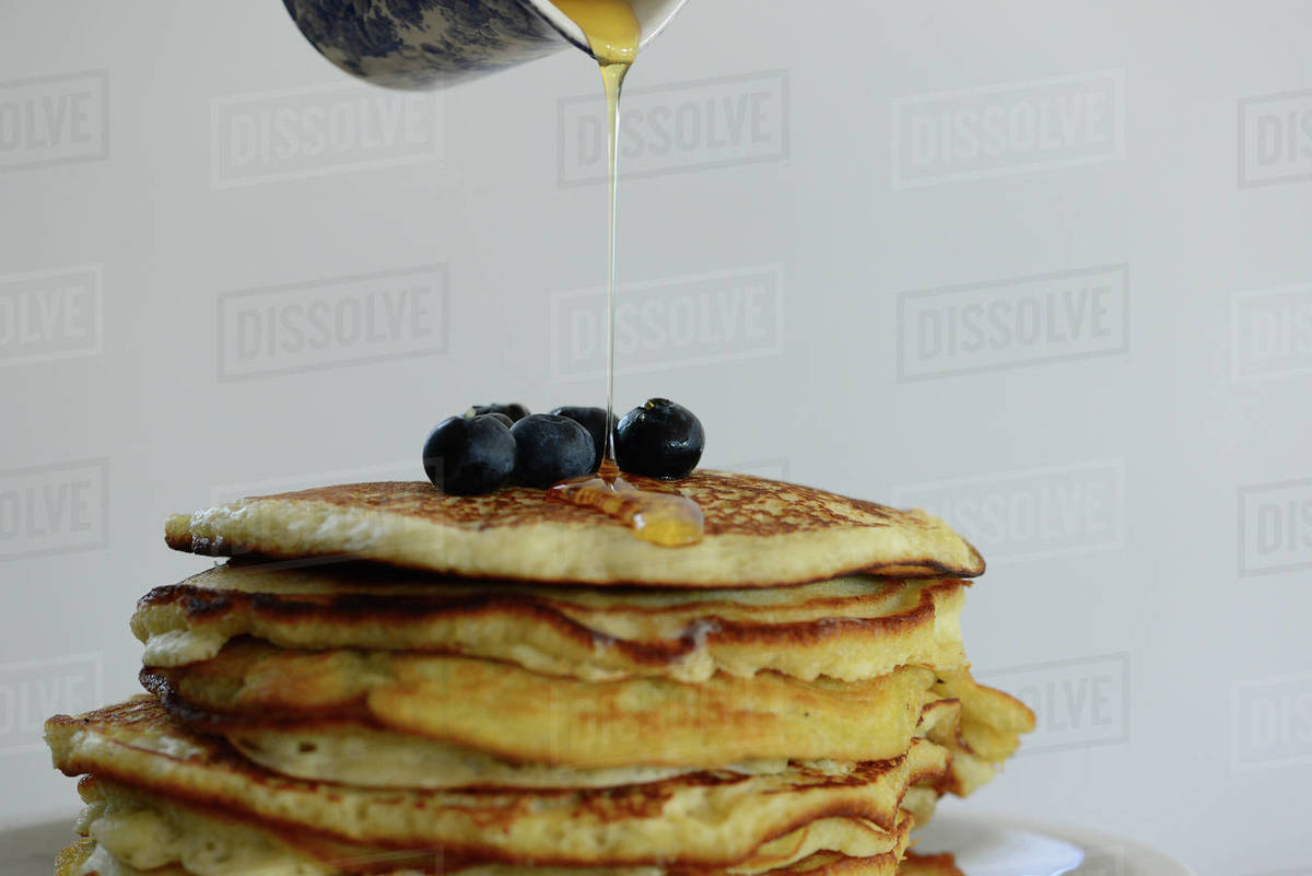 Syrup being poured on a stack of pancakes with blueberries Stock
