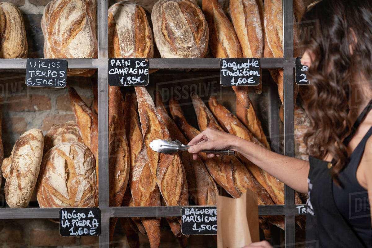 Unrecognizable woman in black apron putting French baguette in paper
