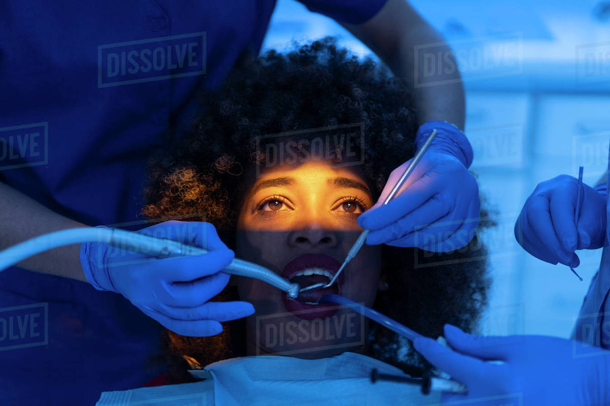 Crop of dentist and assistant using dental suction device on teeth of