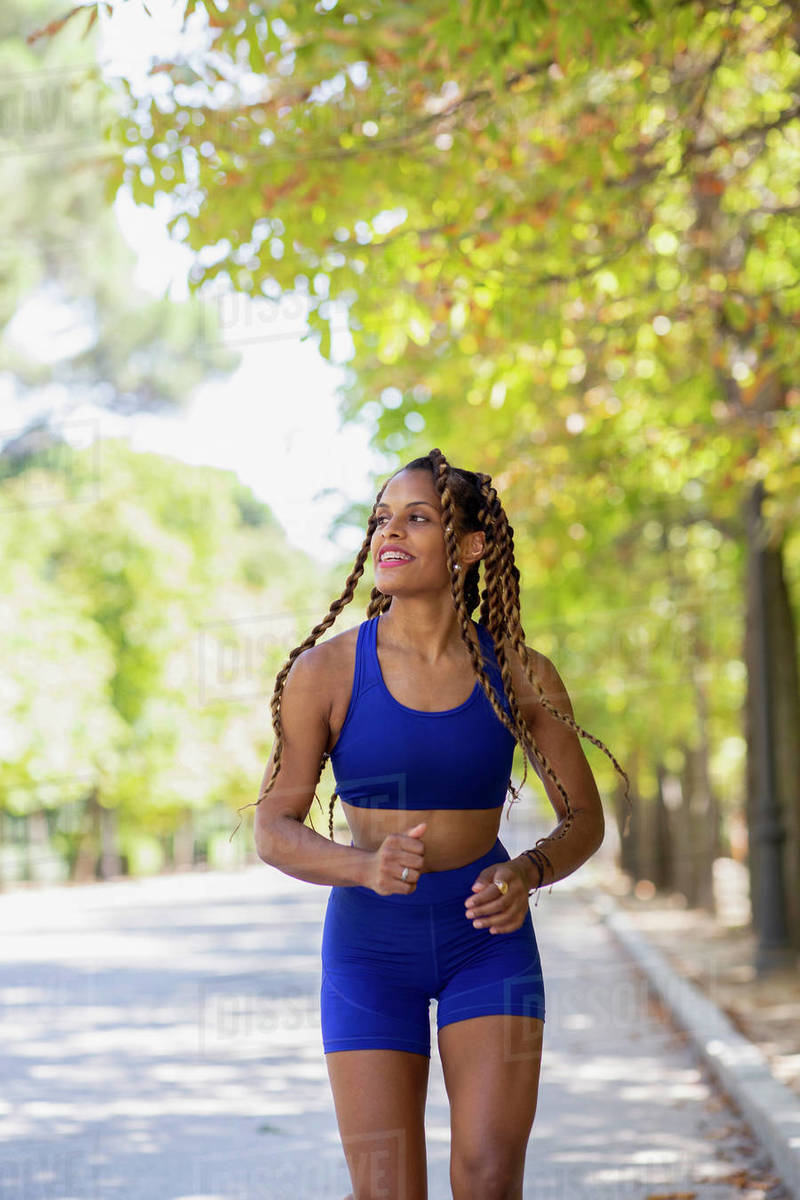 Slim Hispanic female in sportswear running along path in urban