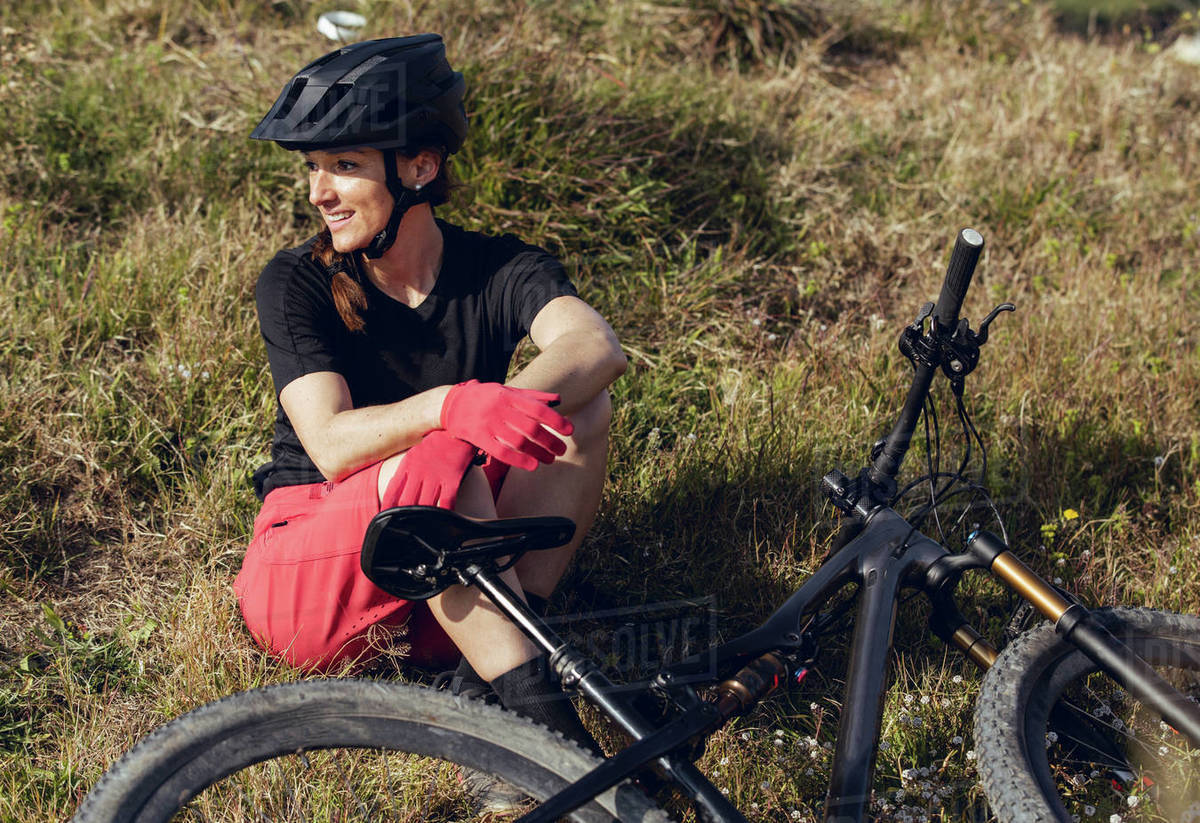 Sportswoman in black helmet and red sportswear sitting resting near training track looking away Royalty-free stock photo