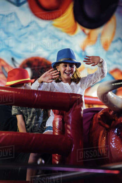 Cheerful girl riding mechanical bull - Stock Photo - Dissolve