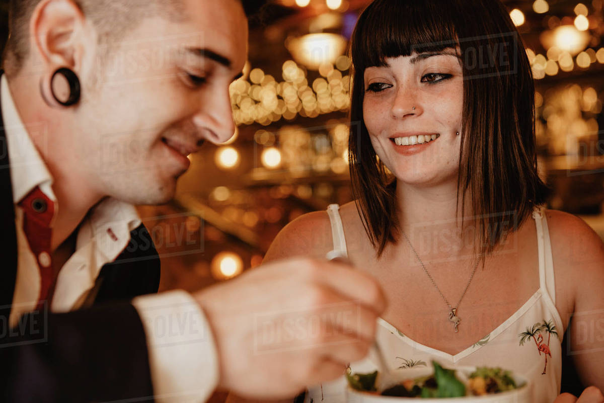 Cheerful young man and woman eating tasty fresh salad while sitting at ...