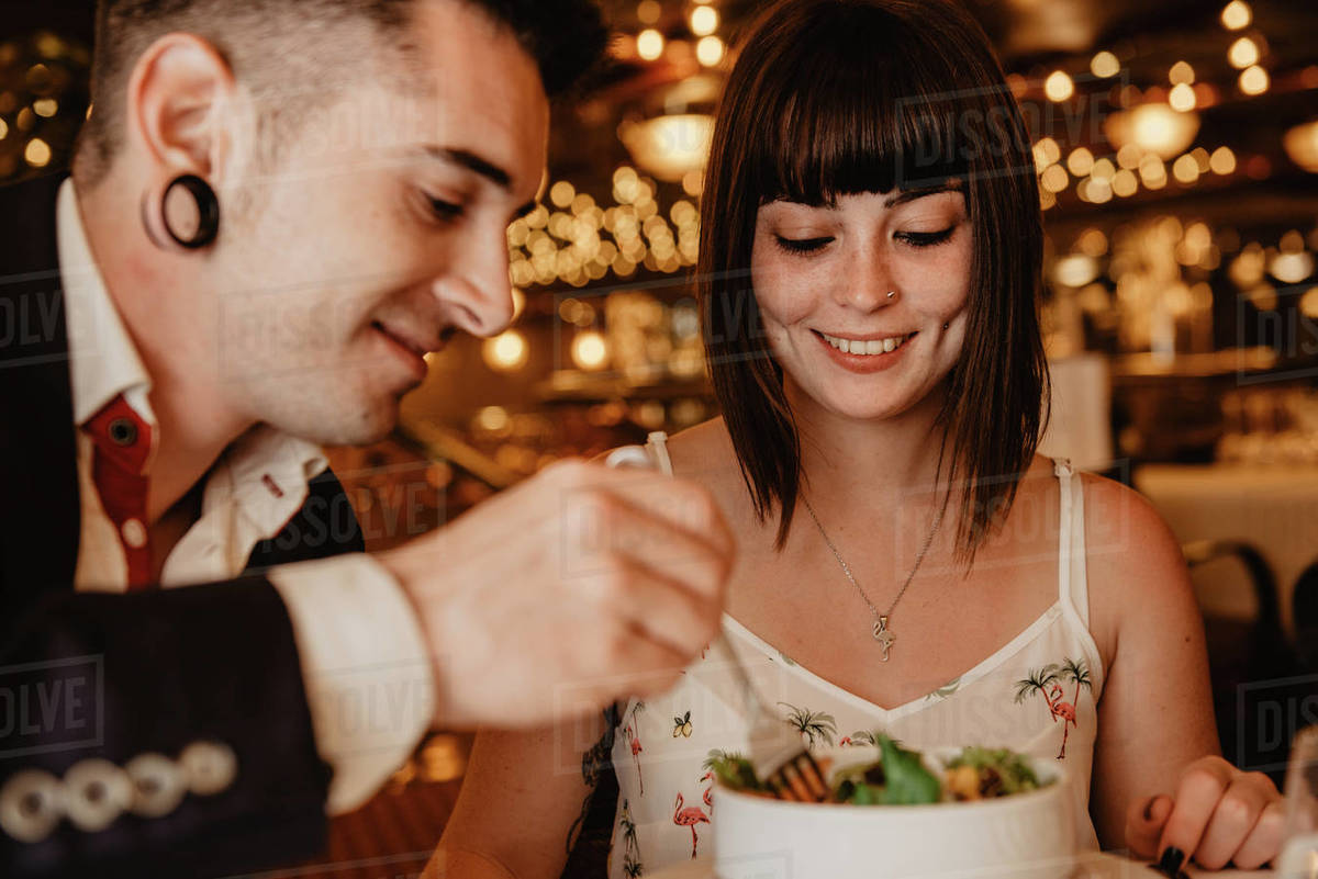 Cheerful young man and woman eating tasty fresh salad while sitting at ...