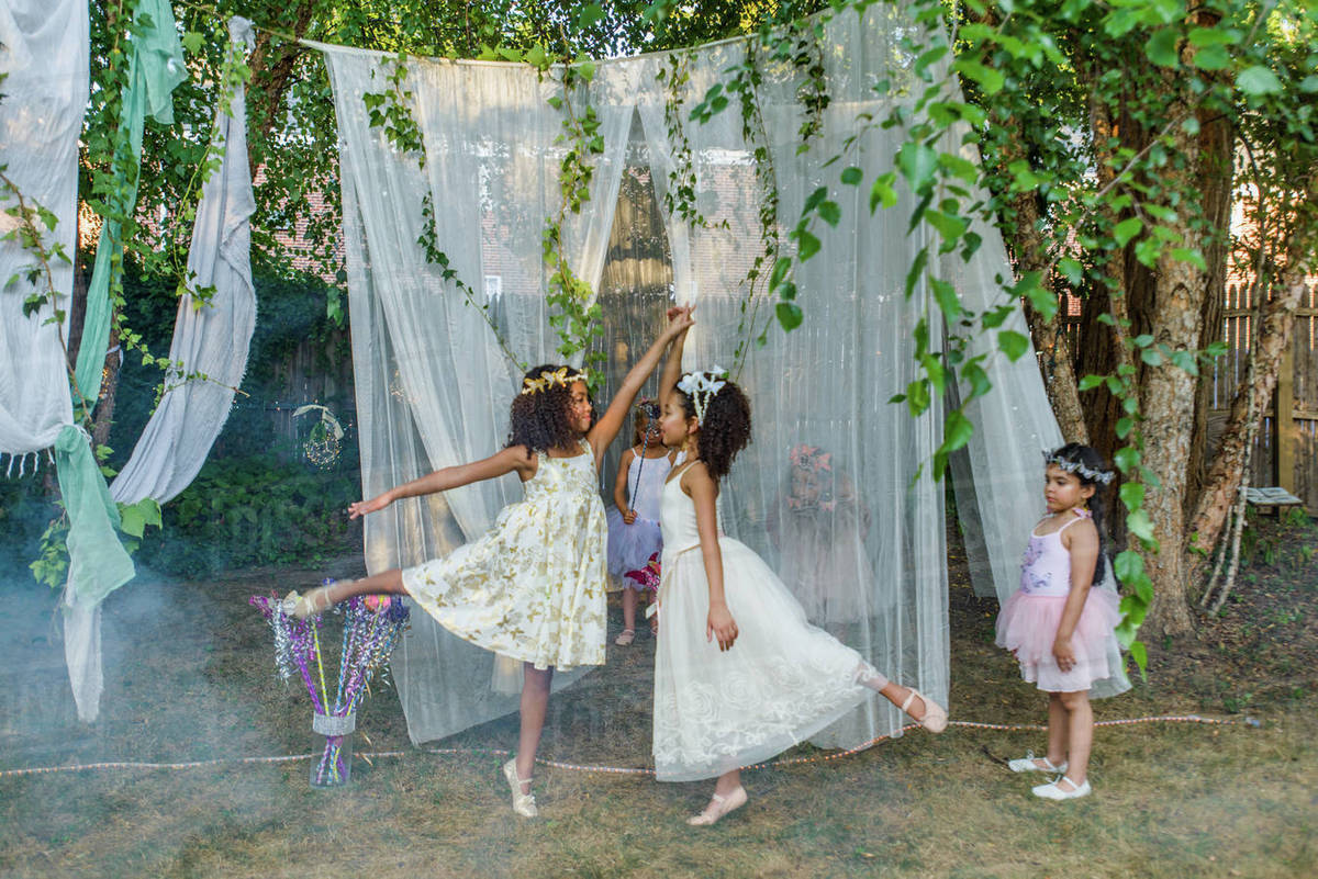 Two young girls, dressed as fairies, dancing outdoors, younger girl watching from side Royalty-free stock photo