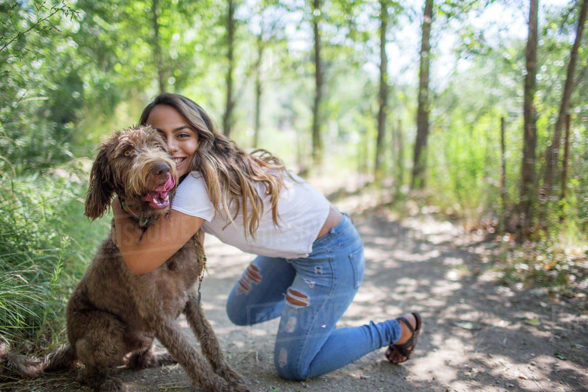 Portrait of teenage girl hugging cute dog on woodland path