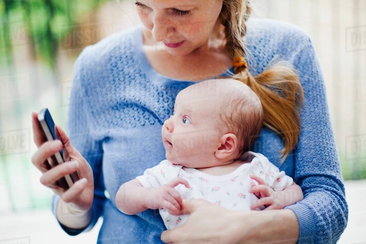 Mother holding newborn daughter and cell phone Stock Photo Dissolve