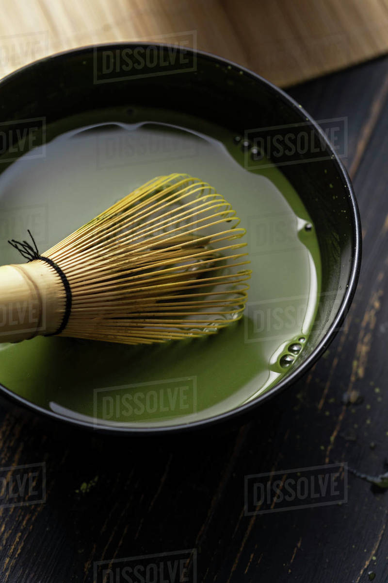 Still life of matcha tea preparation with whisk in bowl of matcha tea