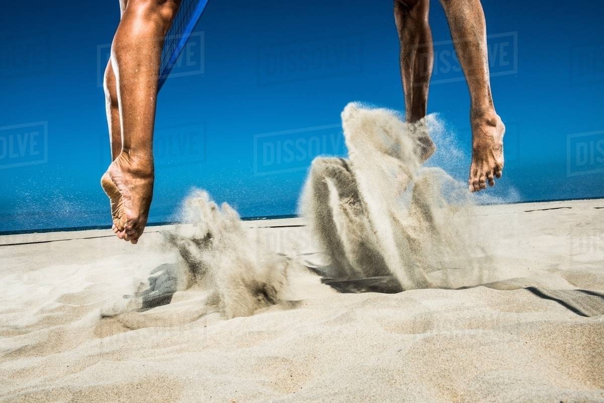 Two beach volleyball players jumping mid air in sand Stock Photo