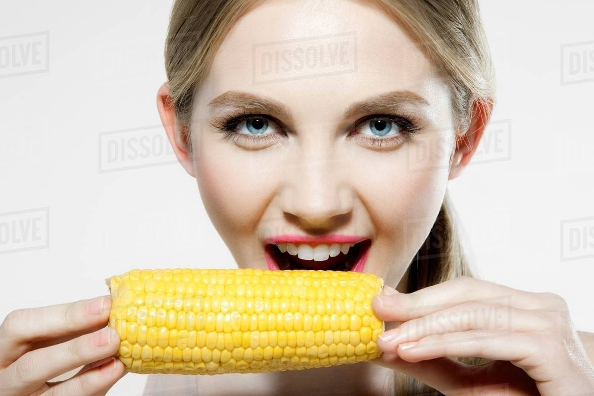Young woman biting corn cob Stock Photo Dissolve