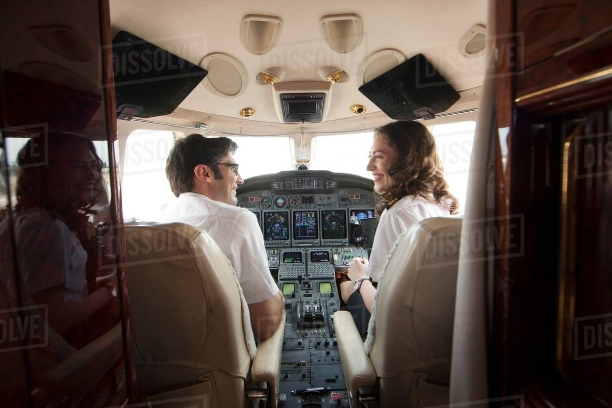 Rear view of male and female pilot chatting in cockpit of private jet ...
