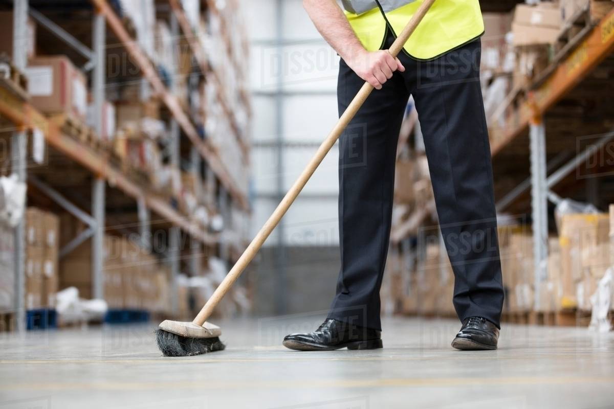 Man sweeping warehouse floor with broom Stock Photo Dissolve