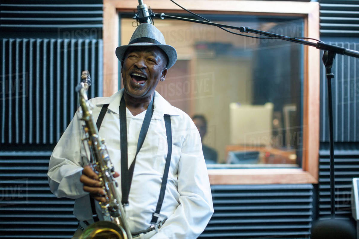 Male musician in recording studio, holding saxophone, laughing Stock