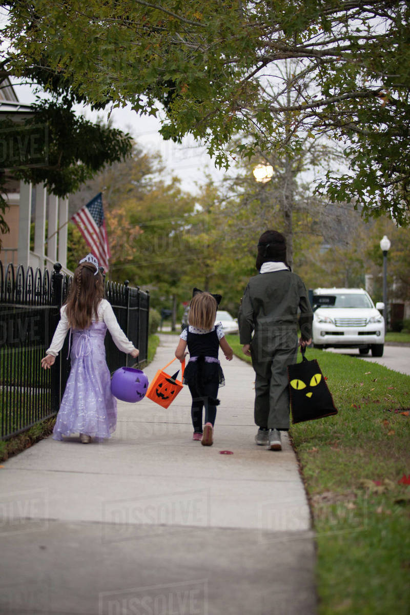 Rear view of boy and sisters trick or treating walking along sidewalk Royalty-free stock photo