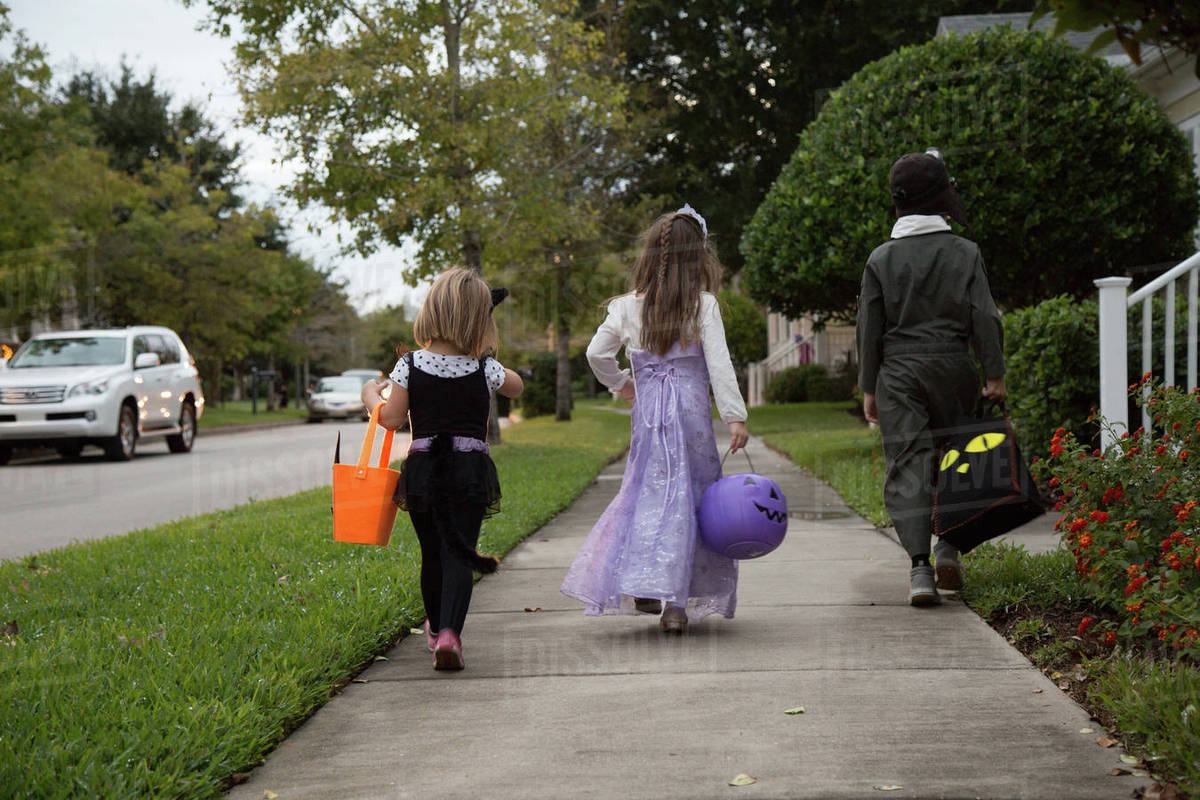 Rear view of boy and sisters trick or treating walking on sidewalk Royalty-free stock photo