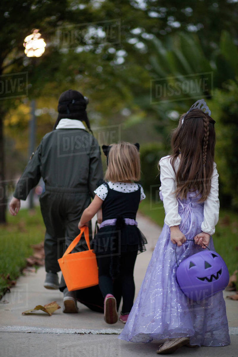 Rear view of boy and sisters trick or treating walking on sidewalk Royalty-free stock photo