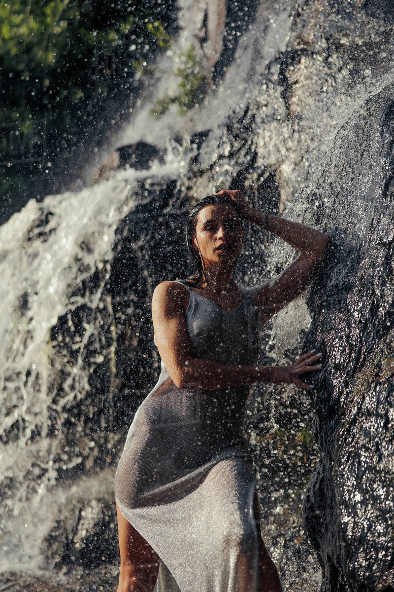 Young woman in wet dress stands near waterfall between water flows, spray and foam. - Royalty-free Stock Photo | Dissolve Young woman in wet dress stands near waterfall between water flows, spray and foam. - Royalty-free Stock Photo | Dissolve
