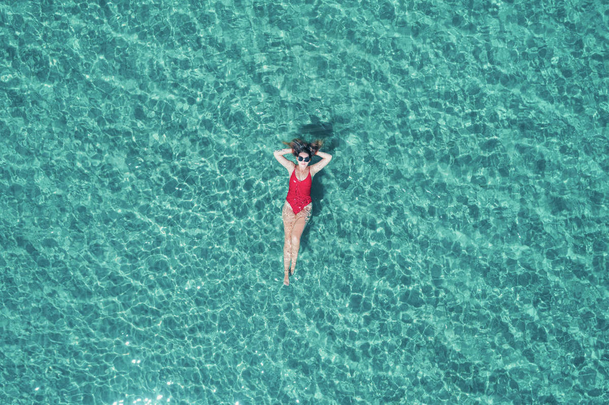 Top view of young pretty sexy girl in red swimsuit floating on water