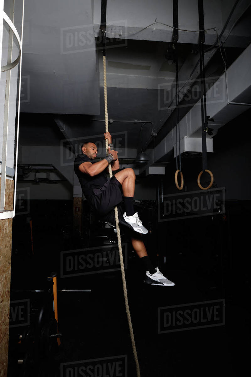 a latin american adult is climbing a rope at the gym with a great