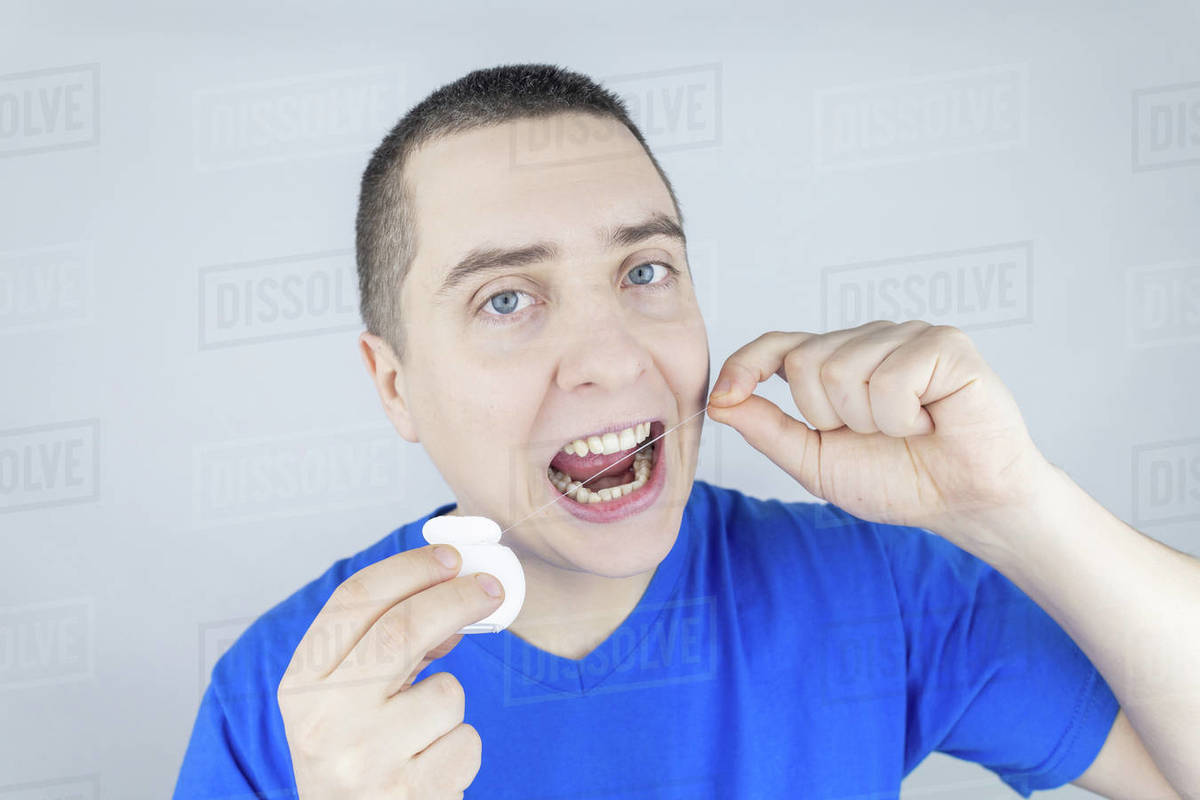 Dental floss close up. A man in front of a mirror brushes his teeth