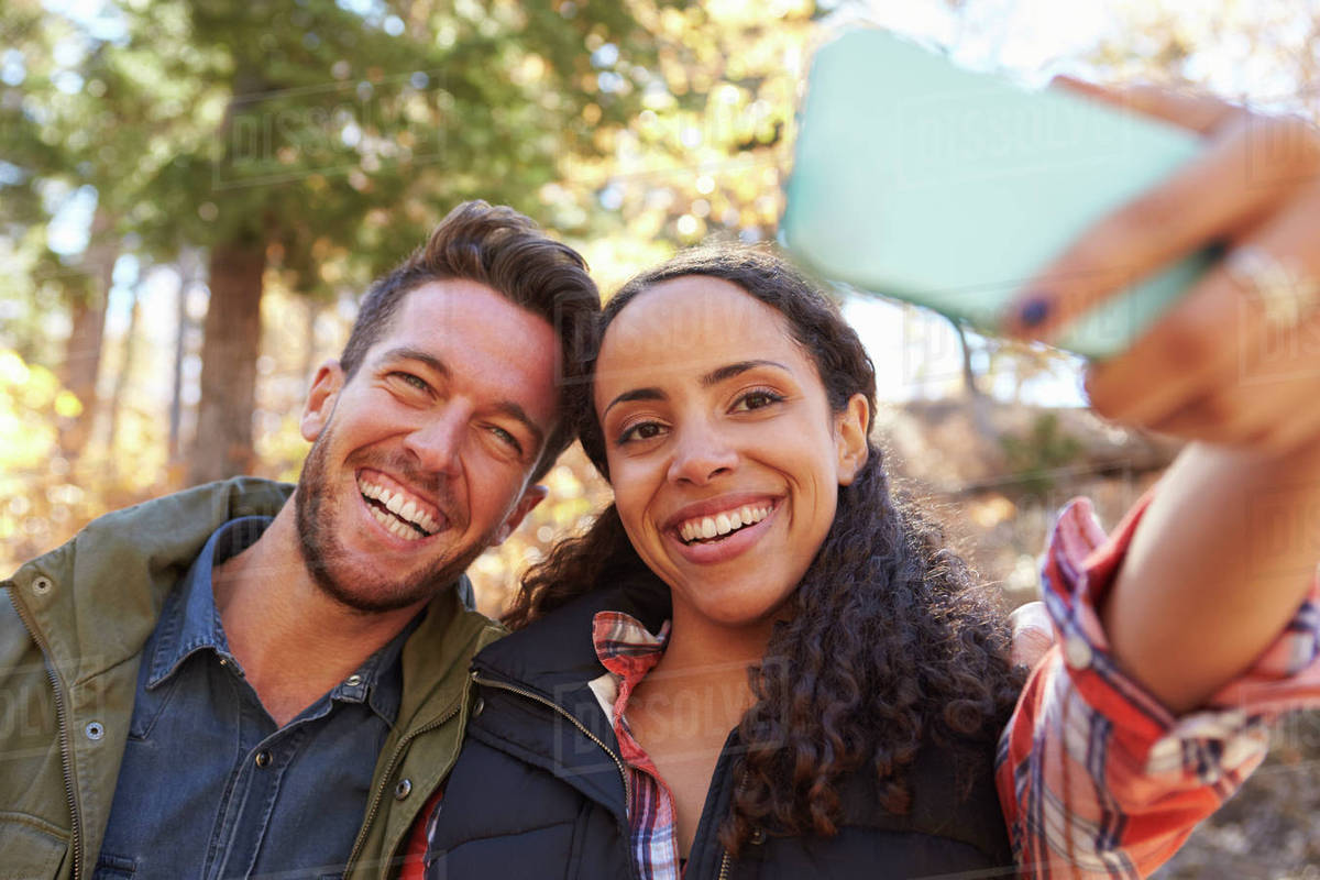 laughing mixed race couple taking a selfie in a forest stock photo