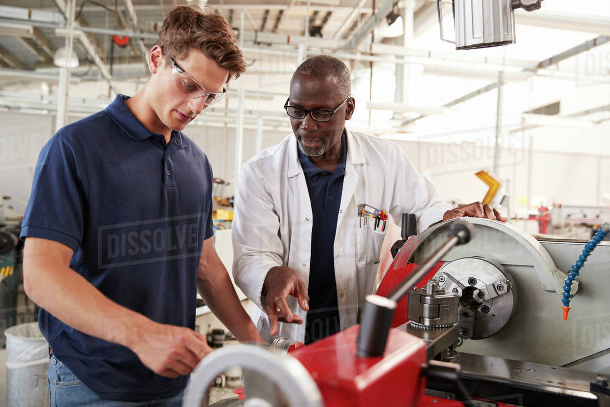 Engineer talking to male apprentice at his workstation, close up Stock Photo Dissolve