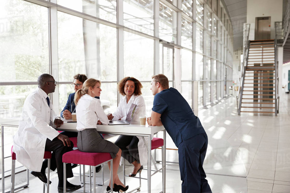 Five Healthcare Workers At A Table In Modern Hospital Lobby