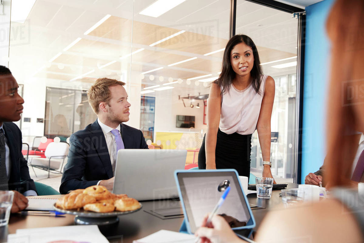 Female boss addressing team in a meeting, over shoulder view Stock