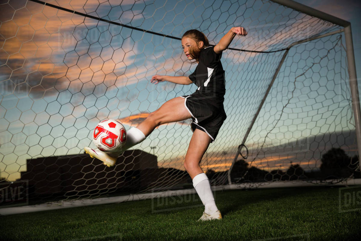 Low angle view of goalie kicking soccer ball in goal under blue sky
