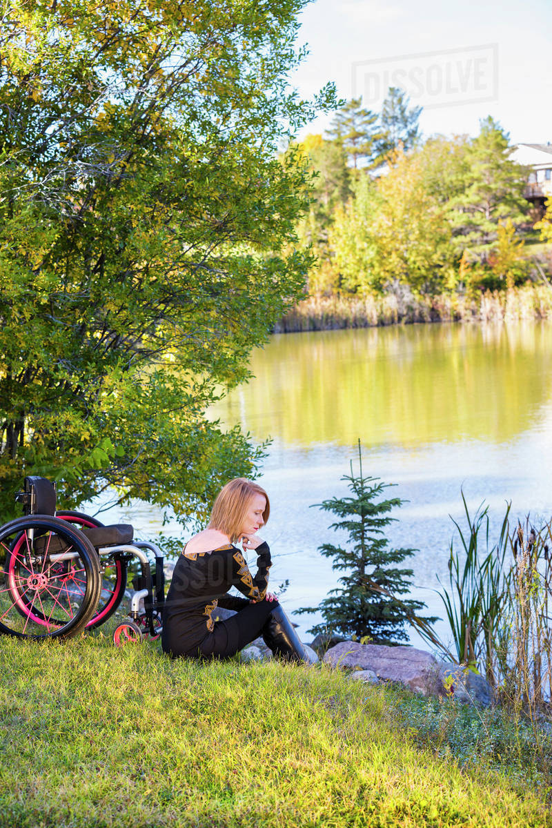Young disabled woman sitting beside her wheelchair in a city park in autumn; Edmonton, Alberta