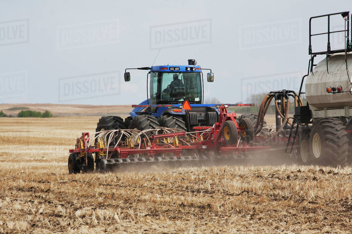 Close Up Of An Air Seeder In A Field With A Tractor And Blue Sky In The