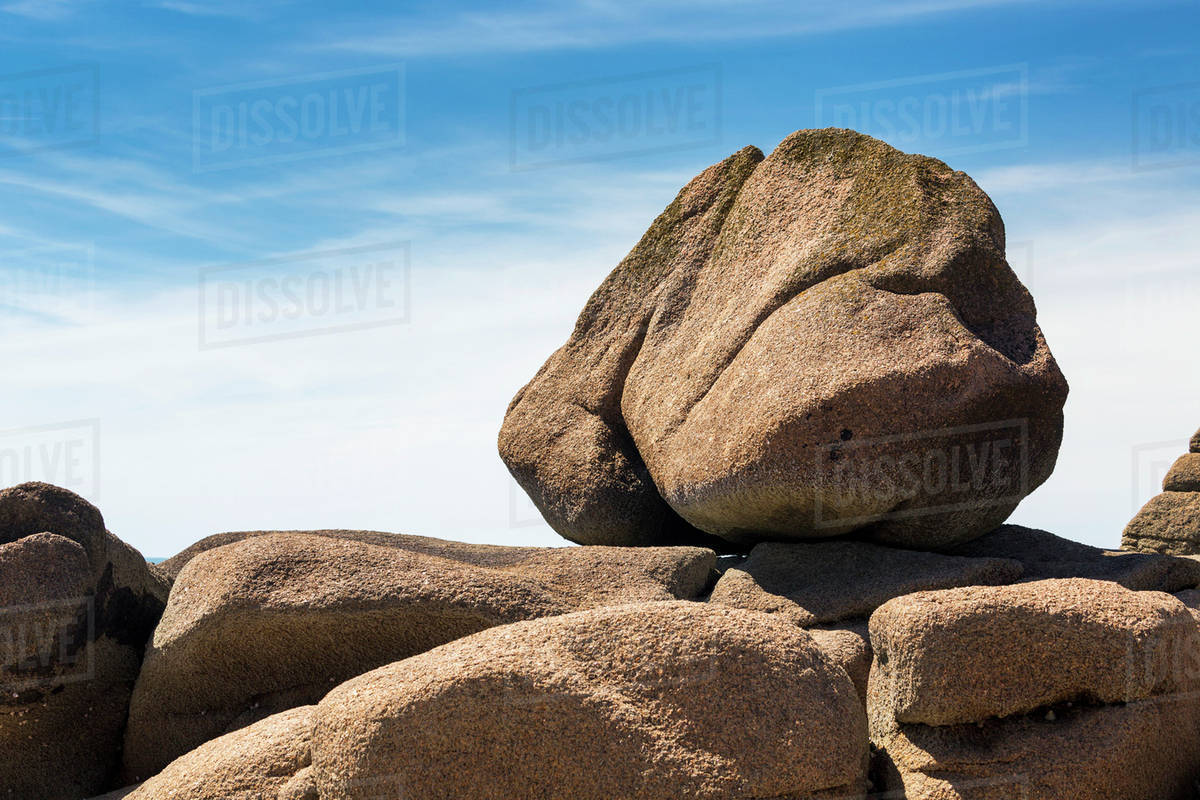 Large round rock balanced on rock formation with blue sky and clouds