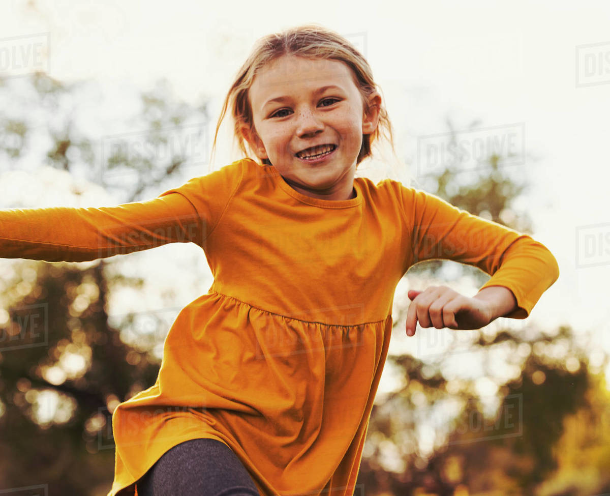 Young girl running across the grass and jumping in the air during a