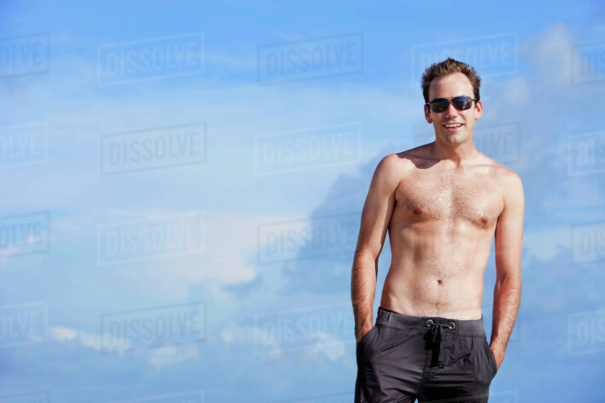 Portrait Of A Man Wearing A Swimsuit And Sunglasses Against A Blue Sky