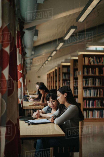 Professor and student discussing over book in library at university ...