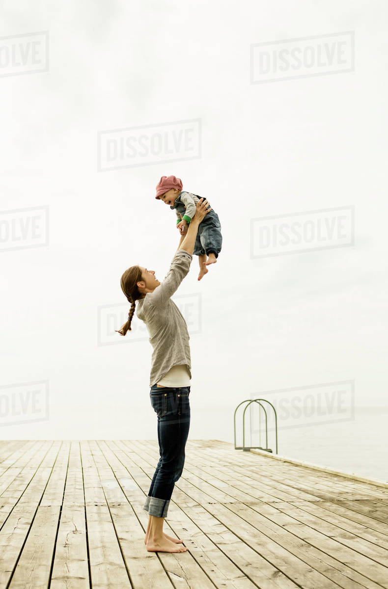 Full length of mother lifting baby girl while standing on pier against