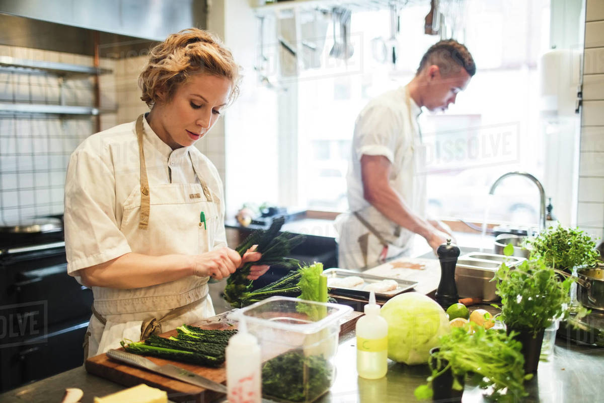 female chef is cutting vegetables by colleague working at counter d929_47_067 restaurant working