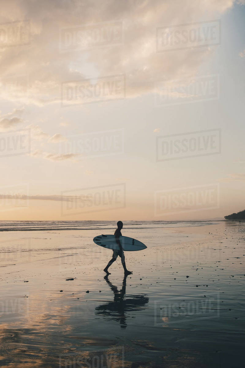 Silhouette man with surfboard walking at beach during sunset Royalty-free stock photo