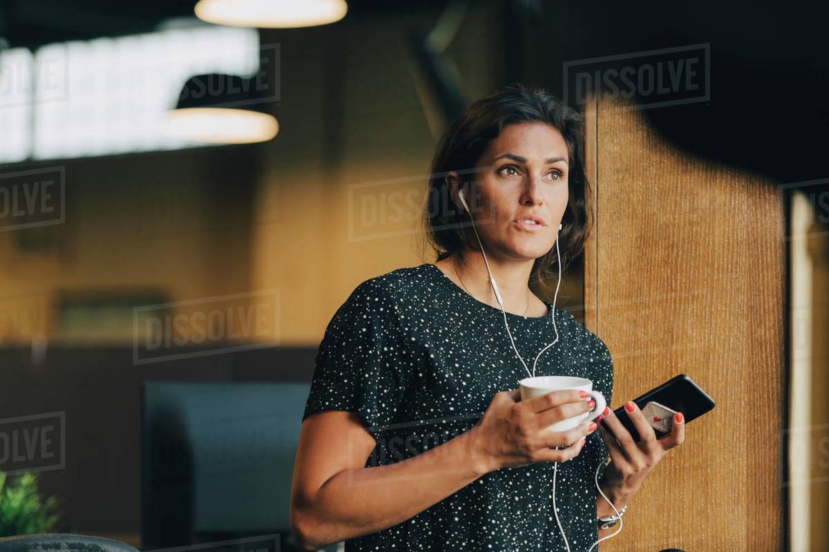 Female executive holding coffee cup while talking with earphones during phone call in office Royalty-free stock photo